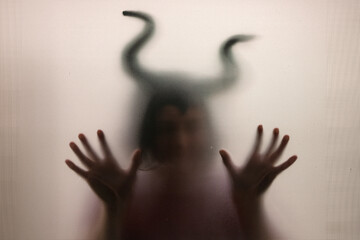 Horror, halloween background - Shadowy figure with horns behind the glass