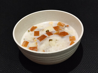 A large bowl of warm angsle, filled with slices of white bread, green beans, white sticky rice and pearls, sprinkled with warm, savory coconut milk sauce, traditional Indonesian food.
