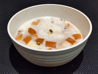 A large bowl of warm angsle, filled with slices of white bread, green beans, white sticky rice and...