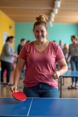 A plus-size white woman is playing table tennis in a bright community center with colorful walls and cheering people. The mood is joyful and lively
