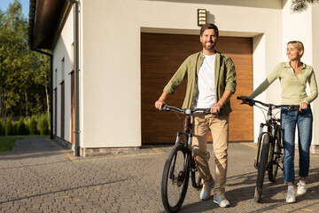 Obraz premium Couple preparing for bike ride outside modern house with garage