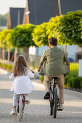 Back view of parent and child enjoying family bike walk on residential trail