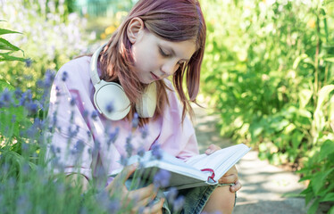 Teenage girl reading a book while wearing headphones in a garden