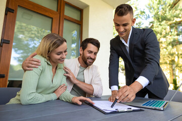 Real estate agent discussing deal with couple on laptop outside home