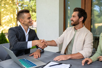 Real estate agent finalizing property contract with couple at outdoor table with laptop and...