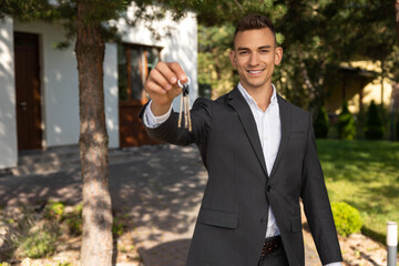 Real estate agent presenting house keys and documents on clipboard in front of property for sale