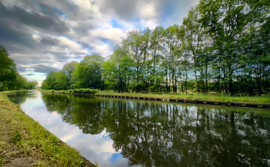 An incredibly peaceful river scene beautifully reflecting the vibrant lush greenery and dramatic, cloudfilled skies