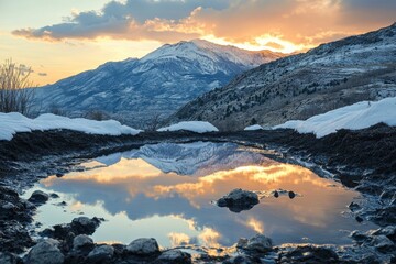 Mountain reflection in a puddle at sunset with snow capped peaks and cloudy sky in the background