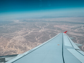 Airplane wing flying over desert landscape with intricate patterns