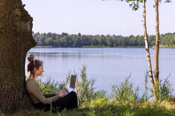 Fototapeta premium A woman enjoys a wonderfully productive day working on her laptop while relaxing by a peaceful lakeside