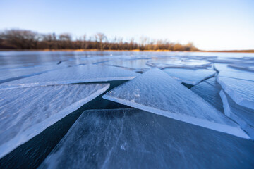 Close up view of cracked ice on a frozen lake with trees in the background under a clear blue sky