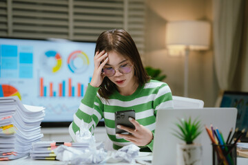 A stressed woman works late at a cluttered desk, surrounded by papers and charts, overwhelmed with...