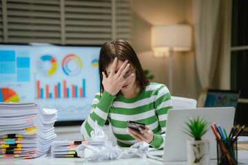 A stressed woman works late at a cluttered desk, surrounded by papers and charts, overwhelmed with...