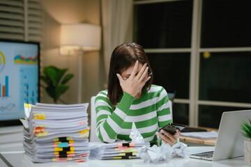 A stressed woman works late at a cluttered desk, surrounded by papers and charts, overwhelmed with...