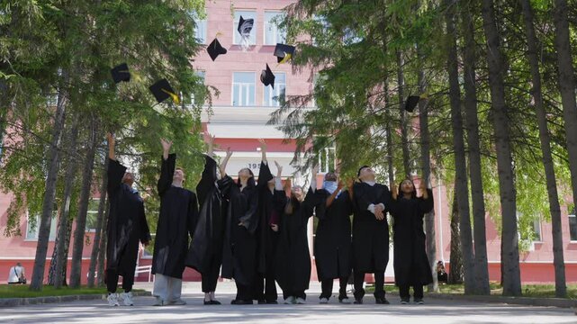 Students of different nationalities in graduation gowns throw their caps in the air. 