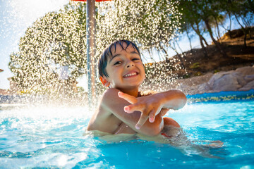 Happy child enjoying refreshing shower in swimming pool on sunny summer day