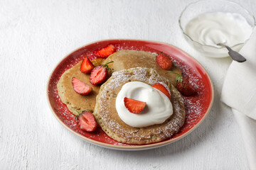 Pancakes with whipped cream or sour cream and fresh strawberries on red plate, sweet breakfast on white background