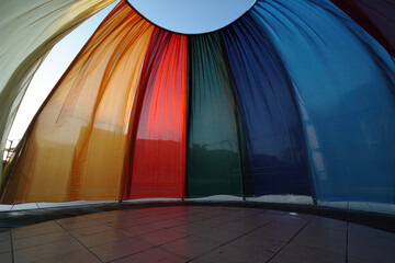 View from inside a colorful tent structure with blue sky visible at the opening at the top