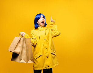 Young girl wearing yellow jacket hold shopping bags and point finger on yellow background. Concept...