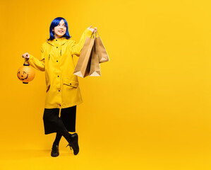Halloween sales. Young girl wearing yellow jacket with shopping bags and halloween pumpkin jack o...