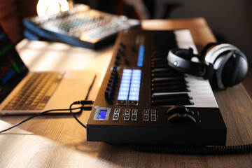 MIDI keyboard with headphones, laptop and dj mixer on wooden table indoors, closeup