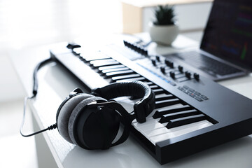 MIDI keyboard, headphones and laptop on white wooden table indoors, closeup