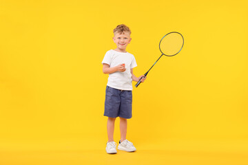 Little boy with badminton racket and shuttlecock on yellow background