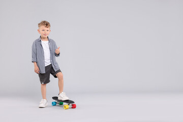 Little boy with penny board showing thumbs up on gray background, space for text