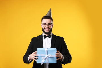 Happy Birthday. Handsome man with party hat and gift box on orange background