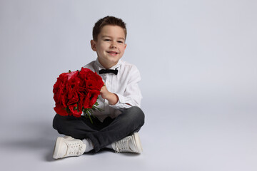 Smiling little boy with bouquet of beautiful flowers on light background