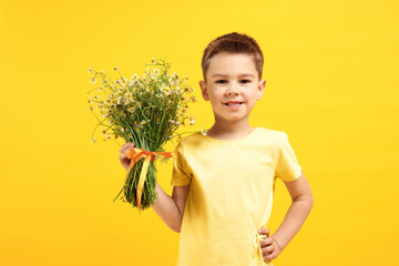Smiling little boy with bouquet of beautiful chamomile flowers on yellow background