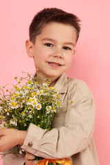 Portrait of smiling little boy with bouquet of beautiful chamomile flowers on pink background
