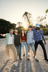 Vertical shot of a happy diverse group of friends walking towards camera at sunset. Concept of...