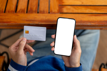 Close up of a man looking at phone holding credit card in hand at wooden table in cafe or canteen.