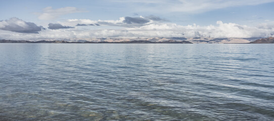 Panorama landscape of Lake Karakul in the Pamir mountains in the Tien Shan against the background of high snowy rocky peaks with clouds, morning panorama of the lake for the background