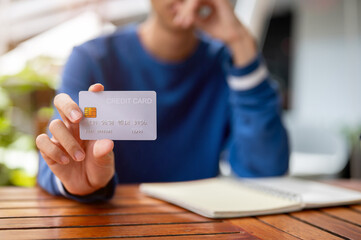 Close up of a man's hand holding or showing a credit card on wooden table in the cafe or canteen.