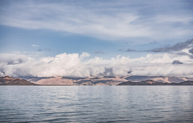 Panorama landscape of Lake Karakul in the Pamir mountains in the Tien Shan against the background of high snowy rocky peaks with clouds, morning panorama of the lake for the background