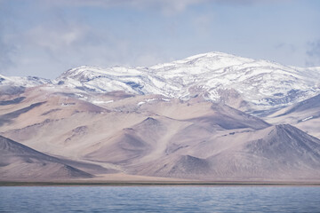 Panorama landscape of Lake Karakul in the Pamir mountains in the Tien Shan against the background of high snowy rocky peaks with clouds, morning panorama of the lake for the background