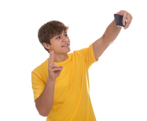 Smiling teenage boy taking selfie by smartphone and showing peace sign on white background