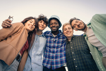 Low angle shot of a happy multiethnic group of friends looking at camera. Concept of friendship, diversity, community and youth lifestyle. A cheerful team embracing and celebrating togetherness. © Lomb