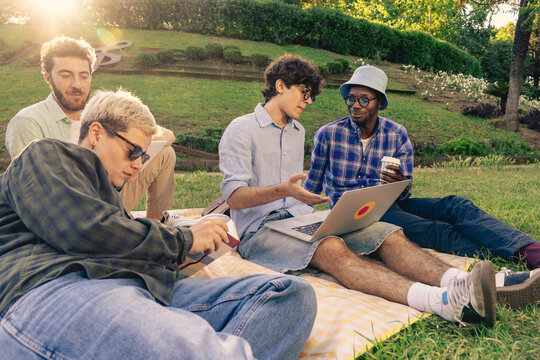 A diverse group of students or young professionals working on a laptop outdoors in a park. Concept of remote work, e-learning, collaboration and modern student lifestyle.