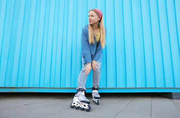 Beautiful young woman with roller skates near light blue wall outdoors, low angle view