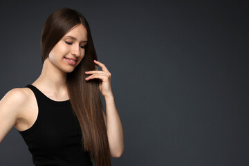 Obraz premium Smiling teenage girl with healthy long hair on dark grey background. Space for text