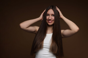 Fototapeta premium Portrait of smiling teenage girl with healthy long hair on brown background