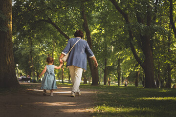 Fototapeta premium Grandmother is walking hand in hand with granddaughter in lush park in the summer 
