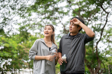 Asian man wiping sweat and holding water bottle with a woman in sportswear after exercising in park