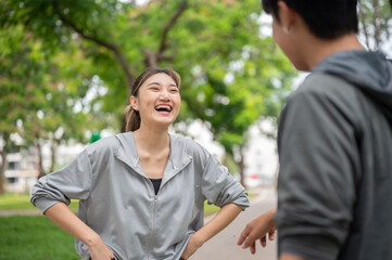 Asian woman in sportswear laughing at a man standing together after running on pavement in the park.