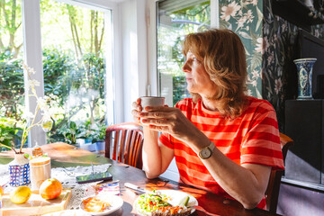 Mature woman enjoying a healthy breakfast with salad and coffee indoors