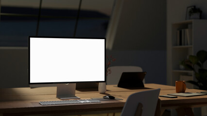 Blank screen computer and tablet with phone and coffee mug on wooden table in meeting room at night
