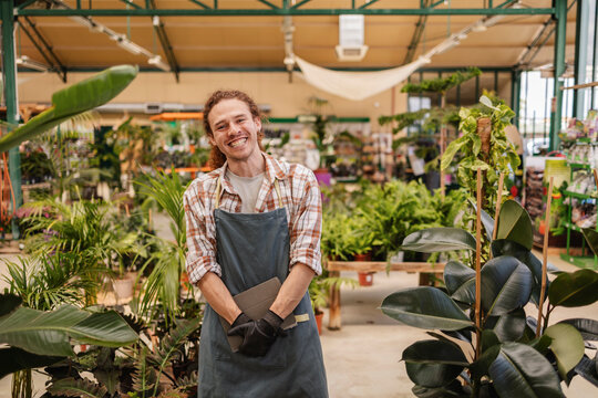 Smiling gardener in greenhouse with plants and apron